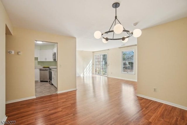 spare room with light wood finished floors, an inviting chandelier, and baseboards