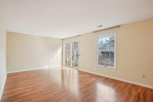 empty room featuring wood finished floors, visible vents, and baseboards