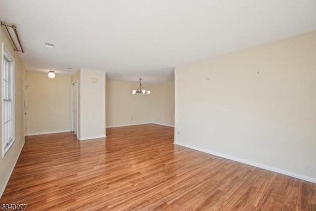 empty room featuring light wood-style flooring, baseboards, and an inviting chandelier