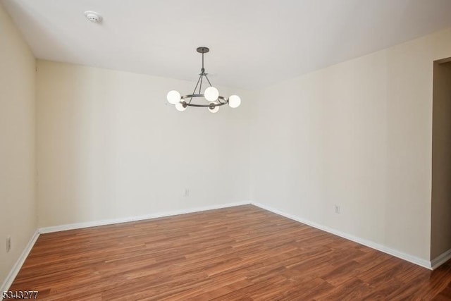 empty room with baseboards, an inviting chandelier, and wood finished floors