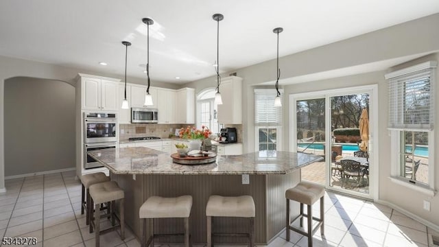 kitchen featuring light stone counters, tasteful backsplash, stainless steel appliances, white cabinets, and light tile patterned flooring