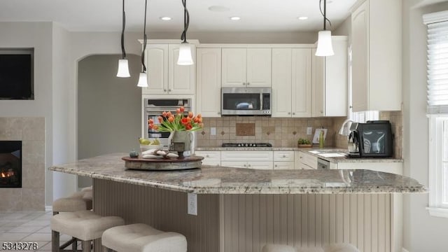 kitchen with white cabinetry, arched walkways, appliances with stainless steel finishes, and a tile fireplace