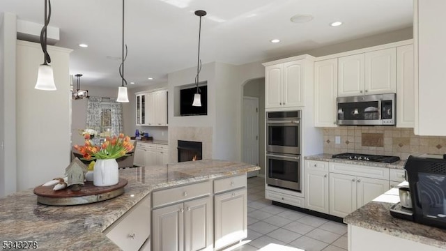 kitchen with stainless steel appliances, arched walkways, white cabinets, light tile patterned floors, and decorative backsplash