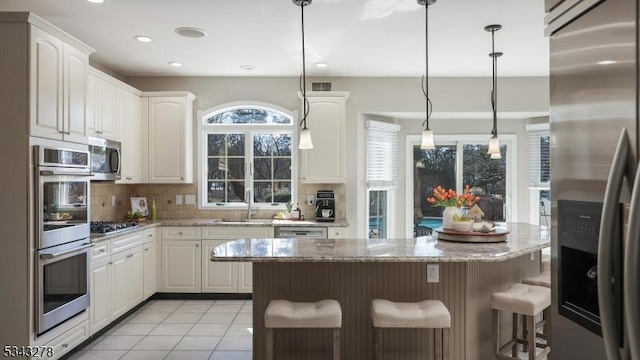 kitchen featuring tasteful backsplash, a kitchen bar, appliances with stainless steel finishes, white cabinets, and a sink