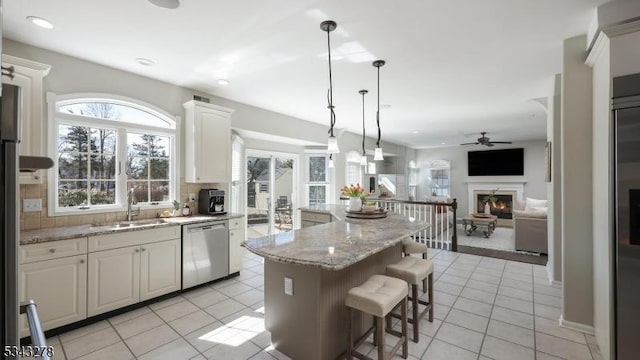 kitchen with a warm lit fireplace, open floor plan, light tile patterned floors, decorative backsplash, and dishwasher