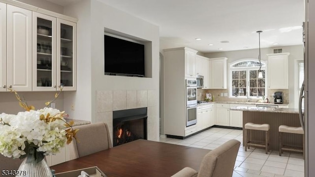 kitchen featuring decorative backsplash, white cabinets, a tile fireplace, and glass insert cabinets