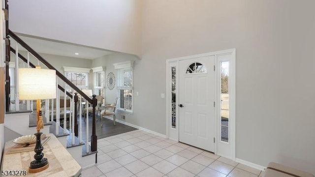 foyer featuring light tile patterned flooring, stairway, a high ceiling, and baseboards