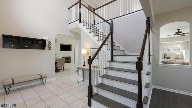 stairs with arched walkways, a fireplace, baseboards, and ceiling fan