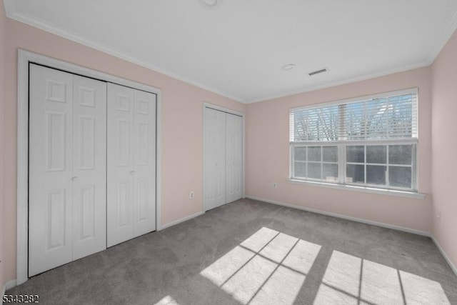 unfurnished bedroom with baseboards, multiple closets, visible vents, and crown molding