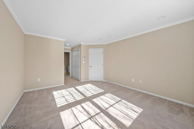 spare room with light colored carpet, crown molding, and baseboards