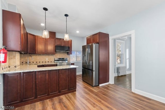 kitchen featuring a peninsula, radiator heating unit, appliances with stainless steel finishes, exhaust hood, and tasteful backsplash