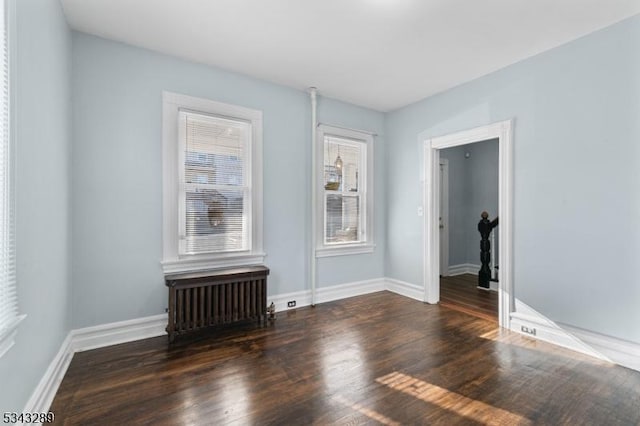 spare room featuring radiator, wood finished floors, and baseboards