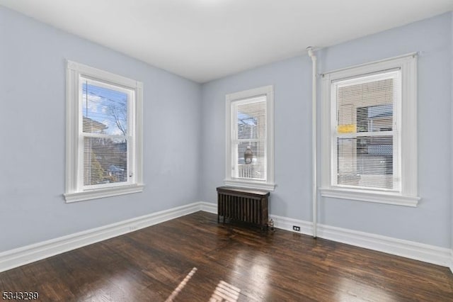 spare room with radiator, wood finished floors, and baseboards