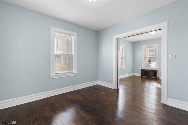 spare room with baseboards, plenty of natural light, wood finished floors, and radiator heating unit