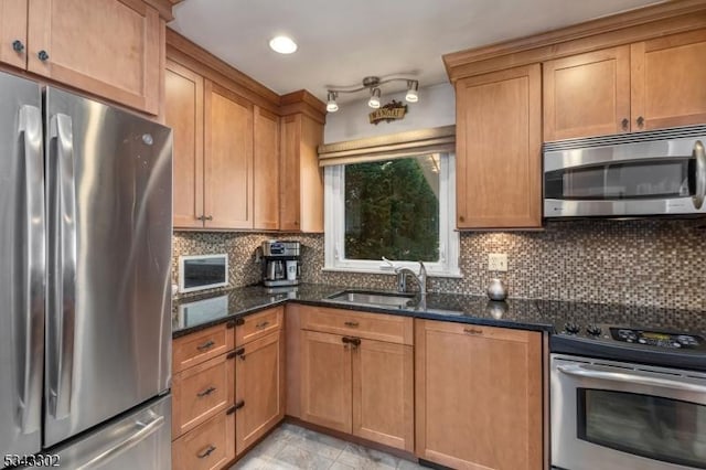 kitchen featuring tasteful backsplash, dark stone counters, brown cabinets, appliances with stainless steel finishes, and a sink