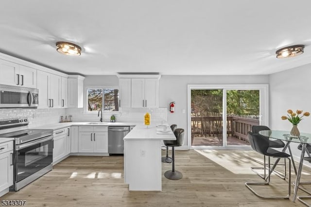 kitchen with light wood-style floors, stainless steel appliances, a kitchen breakfast bar, and backsplash