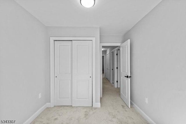 unfurnished bedroom featuring baseboards, a closet, and light carpet