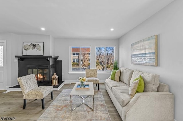 living room featuring a glass covered fireplace, recessed lighting, baseboards, and wood finished floors