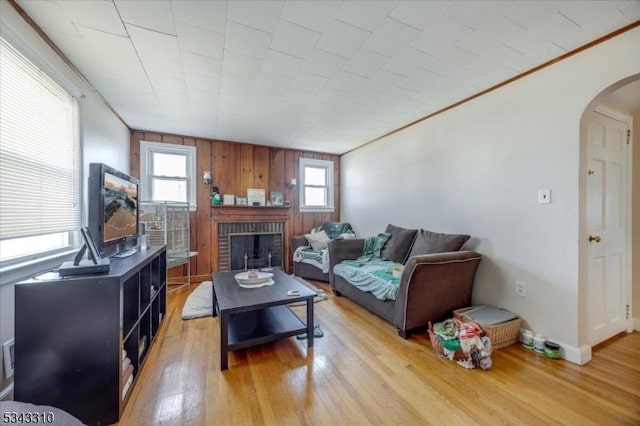 living area with light wood-style flooring, a fireplace, arched walkways, and ornamental molding