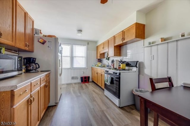 kitchen featuring white gas range, stainless steel microwave, light wood finished floors, and decorative backsplash