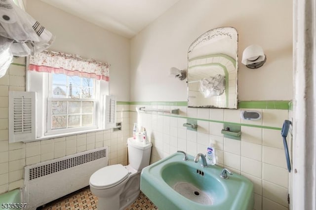 half bath featuring toilet, radiator heating unit, wainscoting, tile walls, and a sink