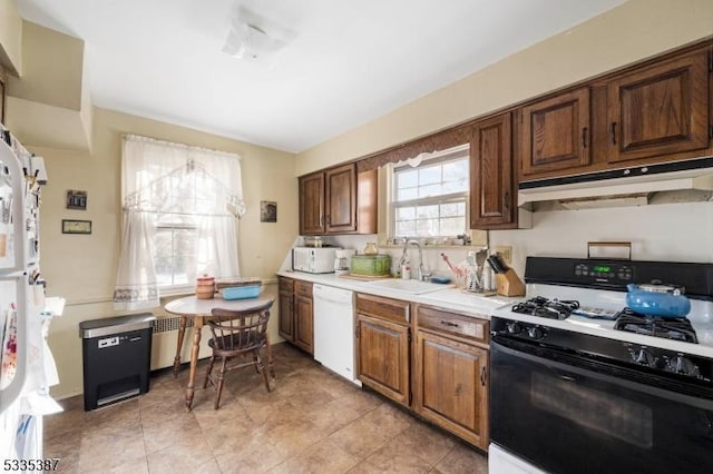 kitchen with under cabinet range hood, light countertops, gas range oven, white dishwasher, and a sink