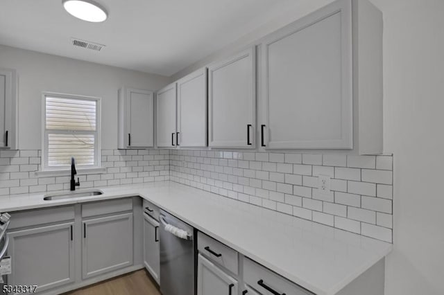 kitchen featuring visible vents, a sink, stainless steel dishwasher, backsplash, and light countertops