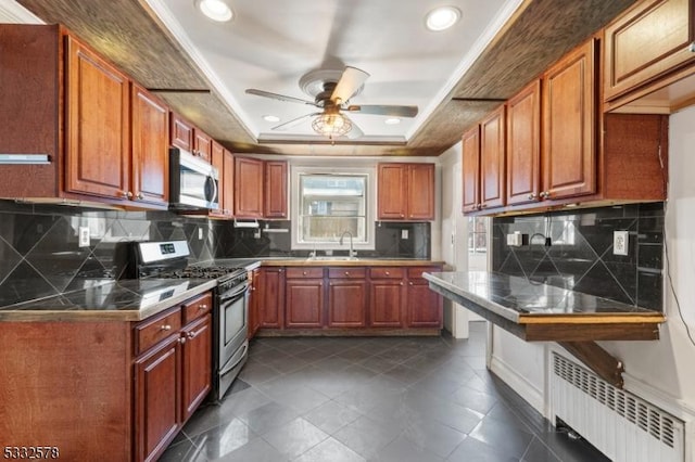 kitchen with radiator, ceiling fan, a tray ceiling, stainless steel appliances, and a sink