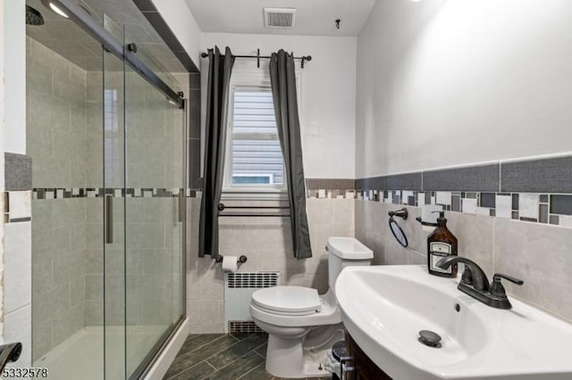 full bathroom with visible vents, radiator, toilet, a stall shower, and tile walls