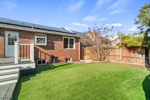 back of property featuring solar panels, a yard, fence, and brick siding