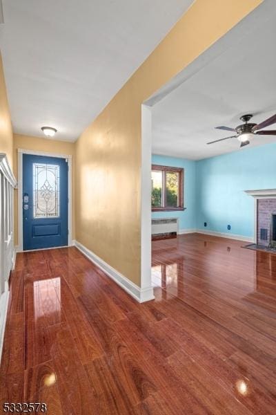 foyer with baseboards, radiator, a brick fireplace, and wood finished floors