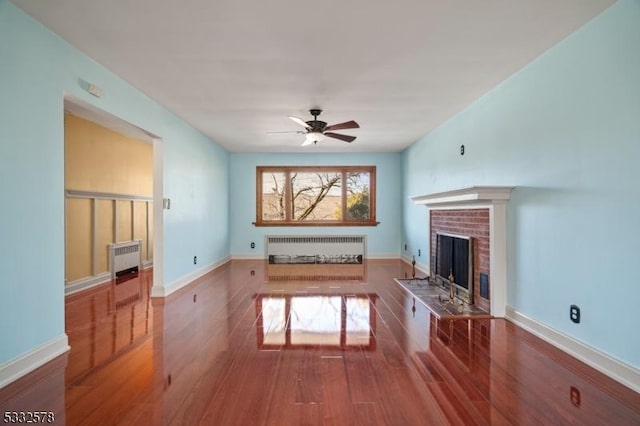 unfurnished living room with radiator, a ceiling fan, wood finished floors, baseboards, and a brick fireplace