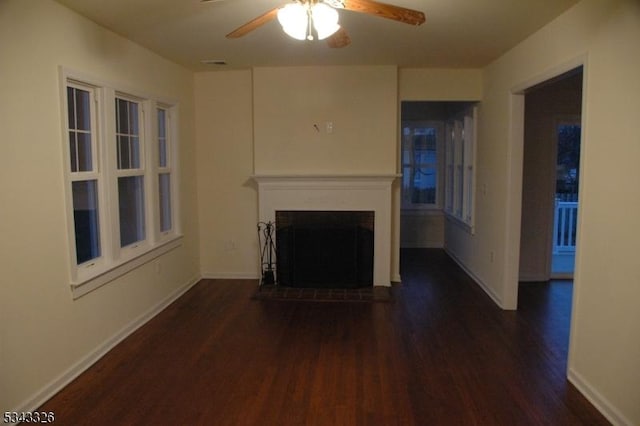 unfurnished living room with visible vents, a fireplace with raised hearth, wood finished floors, baseboards, and ceiling fan