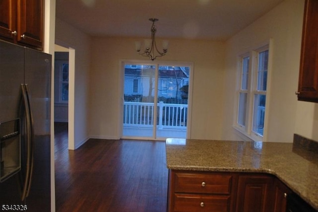 kitchen with dark wood-type flooring, stainless steel fridge with ice dispenser, light stone countertops, a chandelier, and hanging light fixtures