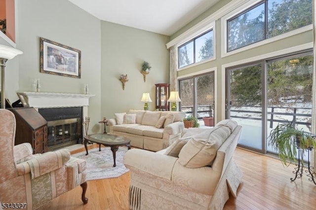 living room featuring light wood-style flooring, a glass covered fireplace, and a towering ceiling