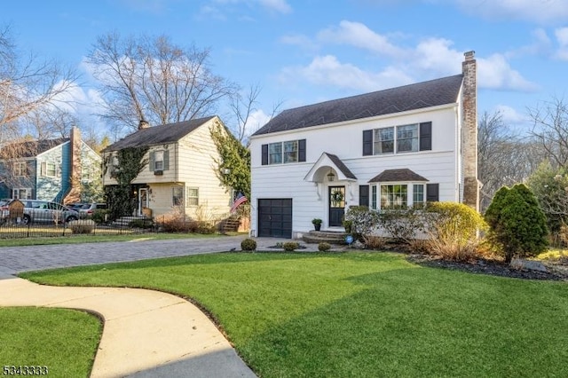 view of front facade featuring a front yard, fence, an attached garage, a chimney, and decorative driveway