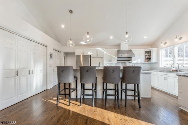 kitchen with wall chimney range hood, a kitchen breakfast bar, freestanding refrigerator, white cabinets, and a sink