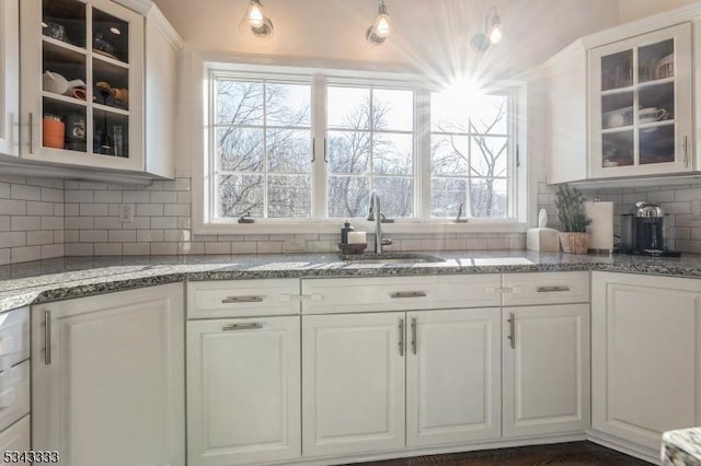 kitchen with a sink, decorative backsplash, light stone countertops, and white cabinets