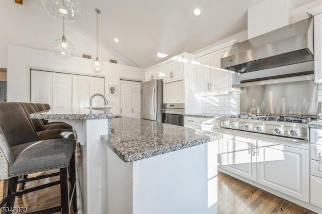 kitchen featuring backsplash, vaulted ceiling, appliances with stainless steel finishes, wall chimney exhaust hood, and a sink