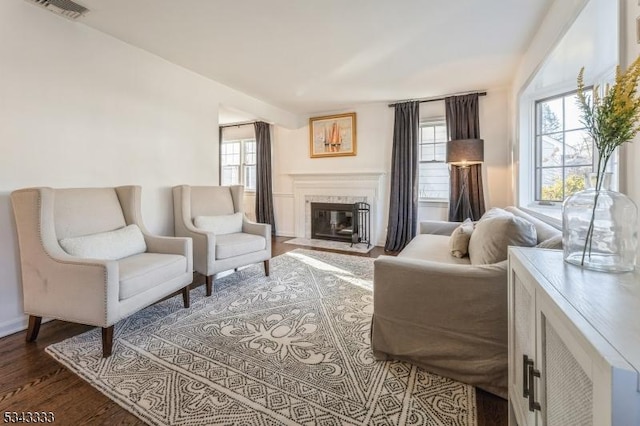 living area featuring a high end fireplace, visible vents, plenty of natural light, and wood finished floors