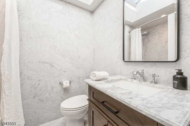 bathroom featuring tile walls, toilet, a skylight, and vanity