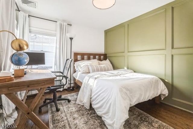 bedroom featuring a decorative wall, wood finished floors, and visible vents