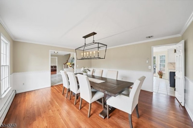 dining area featuring a baseboard radiator, visible vents, wood finished floors, and ornamental molding