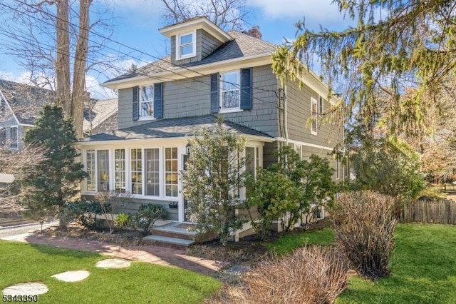 traditional style home featuring a shingled roof, fence, a front yard, a chimney, and a sunroom