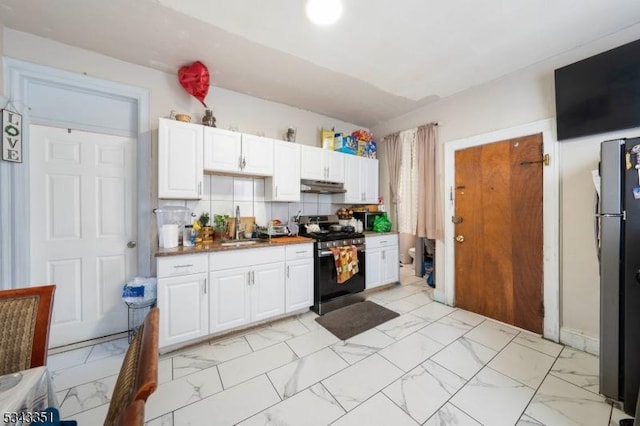 kitchen featuring stainless steel gas stove, marble finish floor, freestanding refrigerator, and under cabinet range hood