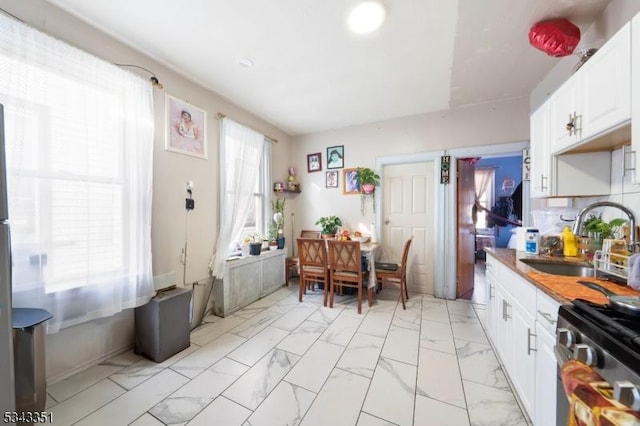 kitchen featuring decorative backsplash, stainless steel gas stove, marble finish floor, white cabinetry, and a sink