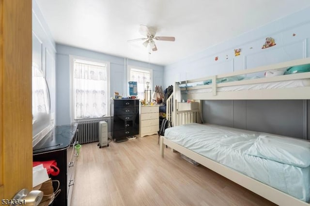 bedroom with a ceiling fan, radiator heating unit, and wood finished floors