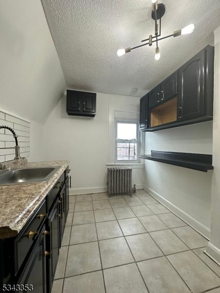 kitchen with a sink, a textured ceiling, radiator, light tile patterned flooring, and baseboards