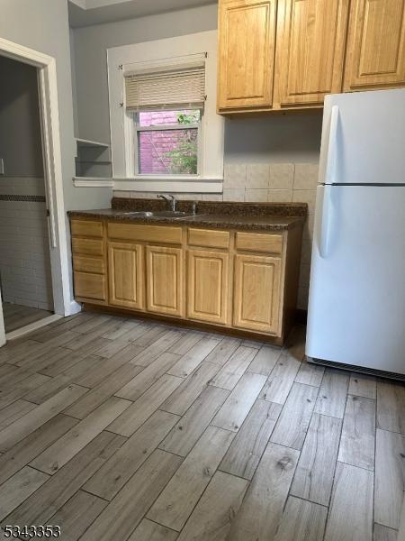 kitchen with dark countertops, light wood-type flooring, freestanding refrigerator, and a sink