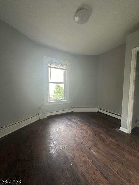 spare room featuring dark wood-style floors, baseboards, and a baseboard radiator